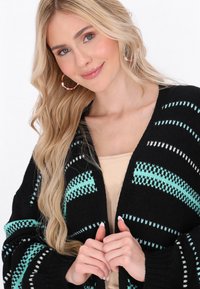 Musta neulecardigan, jossa on turkoosi ja valkoinen raitakuosi, avonainen etuosa, teksturoitu kangas ja rento istuvuus.