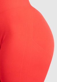 Hoogwaardige leggings in fel koraal, met een gestructureerd patroon aan de zijkant, zachte stof en gevormde naden voor een goede pasvorm.