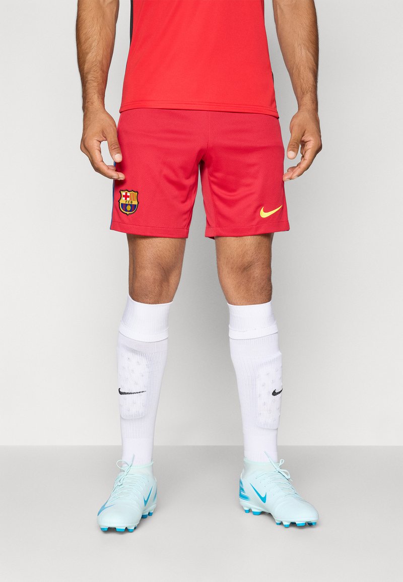 Punaste jalgpallilühikesed püksid Barcelona logo ja kollase Nike swooshiga, millele on lisatud valged sokid ja helesinised jalgpallijalatsid mustade aktsentidega.