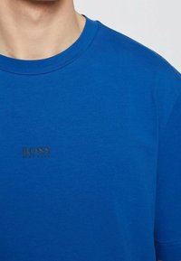 Blå bomulls-t-shirt med rund halsringning och korta ärmar. Har en liten brun "BOSS"-logotyp på bröstet. Slät textur.