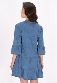 Denim mekko, jossa on kolmannelta neljännekseltä puffihihat, kerroksittain olevat rimat ja pehmeä, teksturoitu vaaleansininen kangas, jossa on pyöreä kaula-aukko.