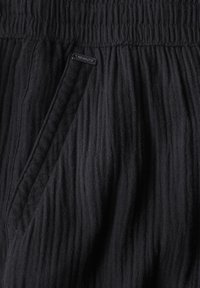 Svarta, texturerade byxor med ett rynkat tyggdesign, med resår i midjan och sidoficka. Liten logotagg på midjan.