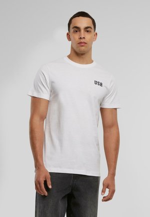 Witte katoenen t-shirt met korte mouwen, ronde halslijn en zwarte "USA" tekst op de borst. Glad materiaal en standaard pasvorm.