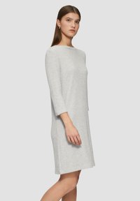 Graues, strukturiertes Kleid mit lockerem Schnitt, rundem Ausschnitt und Dreiviertelärmeln. Das Material wirkt leicht und hat ein gewebtes Muster.