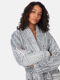 Szary pluszowy szlafrok z geometrycznym wzorem w kolorze białym. Posiada kołnierz typu szalowego i długie rękawy, wykonany z miękkiej i teksturowanej tkaniny.