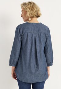 Denimskjorta med en avslappnad passform, trekvartslånga ärmar och detaljer med veck bak. Blått tyg med en jämn textur och rundad nederkant.