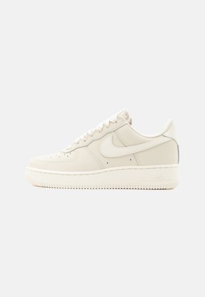 Low-top beige Nike Air Force 1 sneaker with lace-up closure and rubber sole, shown from the outer side on a white background.