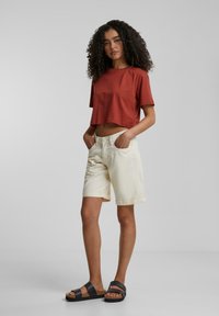 T-shirt enroulé rouillé, shorts crème avec des revers, et sandales noires. Coupe ample avec des manches courtes et poches avant sur les shorts.