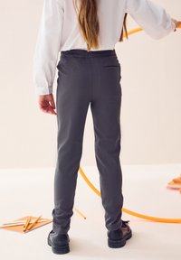 Sivé zužujúce sa nohavice z hladkej látky, s vreckom vzadu, skombinované s čiernymi topánkami.