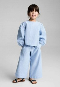 Haut à rayures bleues et blanches à manches longues avec des manches bouffantes, assorti à un pantalon large. Porté avec des sandales marron avec des accents marine.