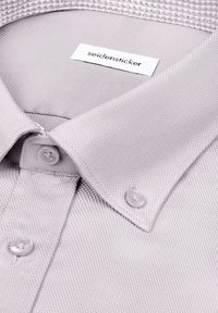 Chemise de ville gris clair texturée avec col boutonné et étiquette blanche portant l'inscription "seidensticker" à l'intérieur du col.