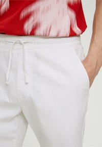 Pantalon à taille élastique blanche avec un cordon de serrage, doté de poches latérales et d'une texture lisse. Le tissu semble léger.