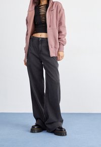 Svart croppad topp med utskärningar, ljusrosa zip-up Hoodie, lösa mörkgrå jeans och kraftiga svarta plattformskängor.