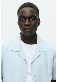 Chemise à manches courtes, bleu clair, en tissu texturé, avec un col cranté et un petit logo brodé.