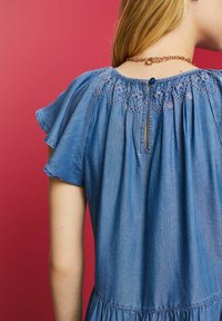 Robe en denim avec des manches courtes flottantes, ornée d'une broderie florale au niveau du col et d'une fermeture par ouverture en goutte d'eau dans le dos. Couleur bleu clair uni.