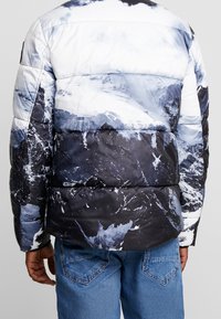 Prošívaná bunda s potiskem horské krajiny v odstínech modré a černé. Má prošívané části a hladký, lesklý povrch.