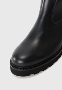 Bota de tobillo de cuero negro con punta redondeada, parte superior texturizada y suela gruesa y resistente. Costuras visibles a lo largo del borde.