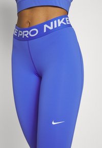 Blå leggings med en vit Nike-logotyp, med en bred elastisk midja med texten "NIKE PRO". Slät yta och åtsittande design.