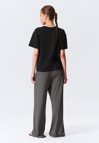 Juoda trumpomis rankovėmis marškinėliai derinami su plačiomis juostuotomis kelnėmis pilkos ir juodos spalvos, turinčiomis laisvą siluetą ir minkštą tekstūrą. Papuošimai apima žiedus.