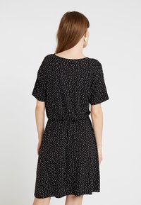 Czarna sukienka z krótkimi rękawami, ozdobiona białym wzorem w kropki, z elastycznym paskiem w talii, sięga do połowy uda. Gładka faktura materiału.