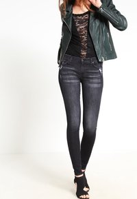 Svarta smala jeans med en urtvättad finish, kombinerade med en svart spetsblus och en mörkgrön läderjacka. Öppen tå svarta kilklackar.