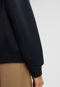 Navy blue sweatshirt made of soft fabric, featuring a ribbed cuff and seam detailing, paired with a light brown textured bottom garment.