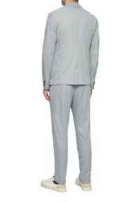 Grau farbener Stoffanzug mit taillierter Passform, ausgestattet mit einem schmalen Revers und passenden Hosen. Kombiniert mit weißen Sneakers, was ein entspanntes Design zeigt.