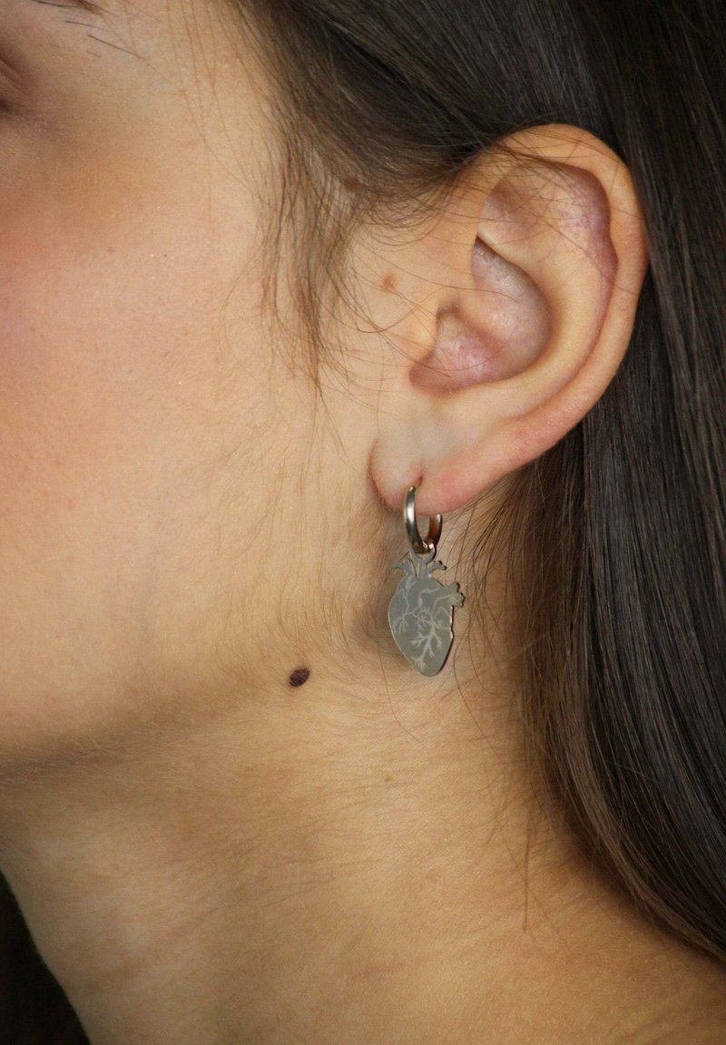 Orecchini in argento a forma di cuore stilizzato, con dettagli intricati. Il design è sospeso da un piccolo cerchio.