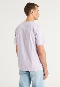 Alyvinė trumpomis rankovėmis marškinėliai, pagaminti iš medvilnės, su tiesiu siluetu ir subtiliu dizainu nugarinėje pusėje. Derinama su šviesiai mėlynomis džinsais.