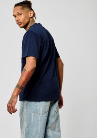 Chemise à manches courtes bleu marine avec un motif géométrique texturé, associée à un short en denim délavé présentant des accents usés.