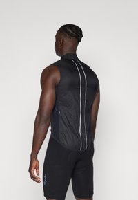 Gilet de cyclisme sans manches noir en matériau léger, doté d'un col haut, de rayures réfléchissantes blanches et d'une poche latérale zippée.