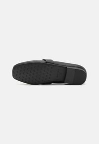 Scarpa nera slip-on con suola piatta e un motivo di grip testurizzato, materiale superiore liscio e un discreto logo in rilievo.