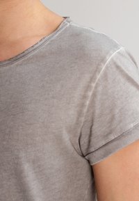 Šedé tričko s krátkým rukávem a kulatým výstřihem. Měkký, mírně texturovaný materiál s komfortním střihem a minimalistickým designem. Úhledné švy.