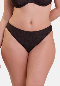Femme portant un bas de bikini brun foncé pailleté et un haut assorti, vue de la mi-torse jusqu'à la partie supérieure des cuisses sur un fond uni.