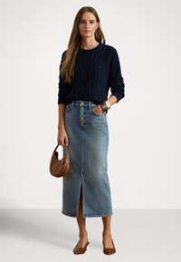 Μπλε πουλόβερ με πλεκτό υφή, σε συνδυασμό με μια τζιν φούστα μεσαίου μήκους, με σχίσιμο στο μπροστινό μέρος και κούμπωμα με κουμπιά. Καφέ τσάντα χειρός και παπούτσια.
