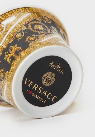 Keramiikkakuppi musta-kultaisella barokkiprintillä, jossa valkoinen reuna. Pohjassa näkyy "VERSACE"-logo ja tunnus, jossa on yksilölliset yksityiskohdat.
