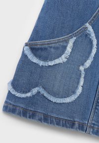 Denimkangas keskmises sinises, millel on kaks frantsiisitud taskut, millel on laineline äärise disain. Kontrastses värvitoonis õmmeldud peened õmblused rõhutavad vormi.