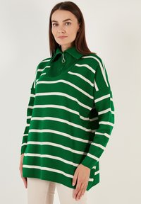 Groen en wit gestreepte pullover met een halve rits kraag. Heeft een ontspannen schouder en een relaxte pasvorm in een zachte, geribde breistekstuur.