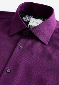 Paarse gestructureerde op maat gemaakte dress shirt met zwarte knopen en een bloeiende binnenkraagvoering, gelabeld "NEXT Tailoring."