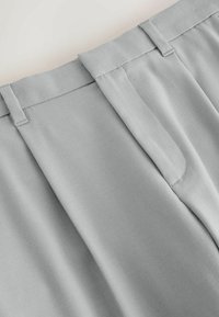 Light grey tailored trousers with a smooth fabric texture, featuring a flat waistband and neatly stitched details.