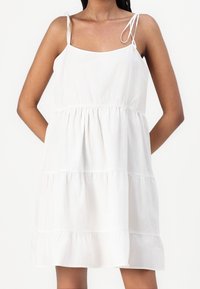Biała bawełniana sukienka z regulowanymi ramiączkami, kwadratowym dekoltem i warstwowym wykończeniem w falbanki, charakteryzująca się luźnym krojem i gładką fakturą.