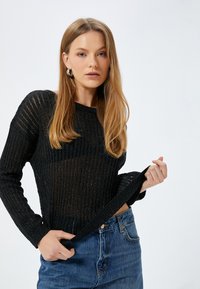 Svart ribbad stickad tröja med långa ärmar, med en strukturerad design, rund krage och smal passform, som kombineras med högmidjade denimjeans.