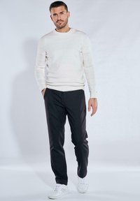 White striped sweater, black pants, and white sneakers. The sweater features a round neck and subtle texture. Pants have an elastic waistband.