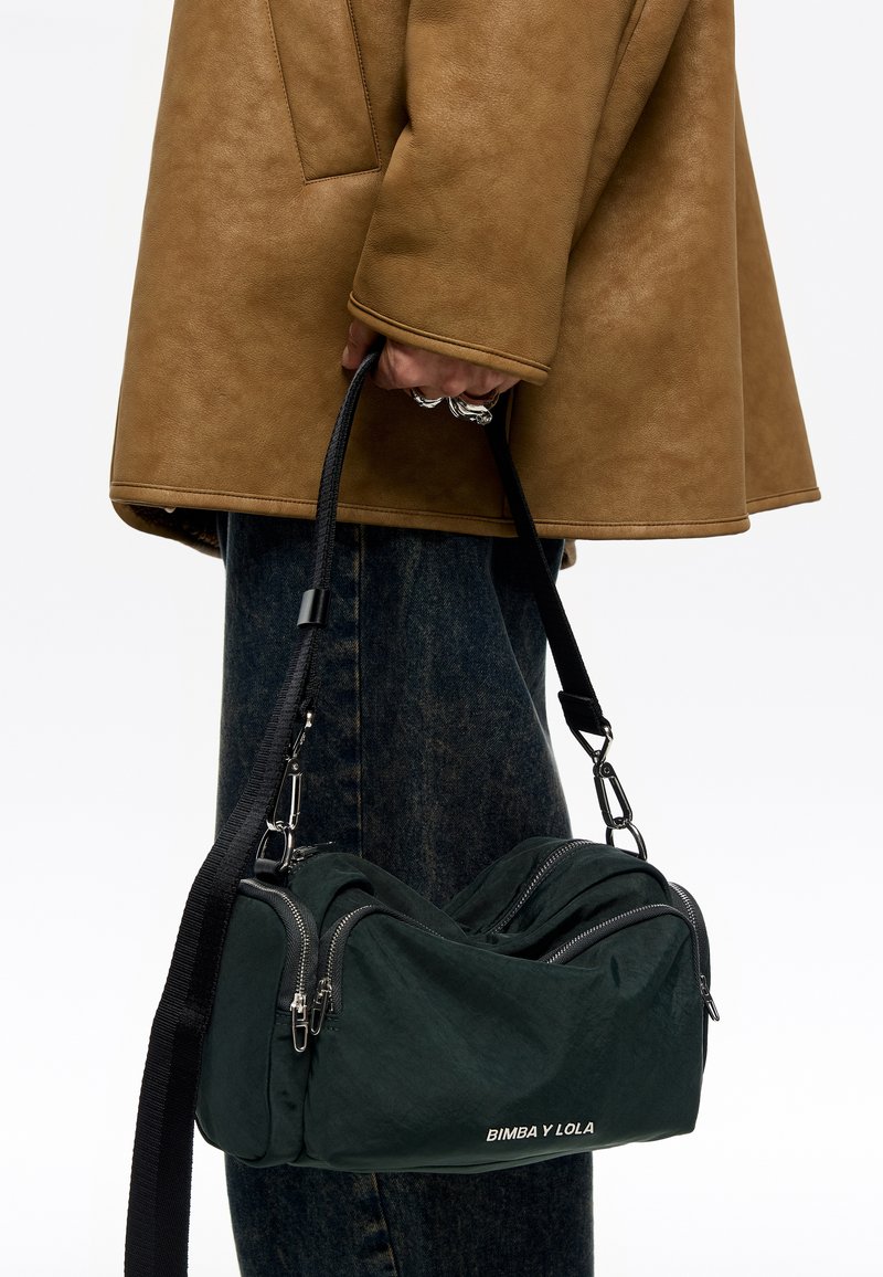 Bolsa de tela verde oscuro con dos compartimentos con cremallera, correa negra y herrajes plateados. Logo "BIMBA Y LOLA" en la parte frontal.
