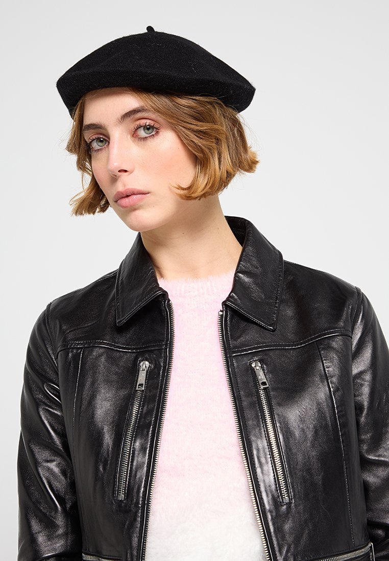 Czarna wełniana beretka, dopasowana skórzana kurtka z zamkami błyskawicznymi w kieszeniach oraz miękki różowy sweter, przedstawiający zbliżenie twarzy modelki.