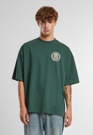 Green oversized short-sleeve t-shirt made of cotton with a round neckline and a circular graphic design on the left chest.