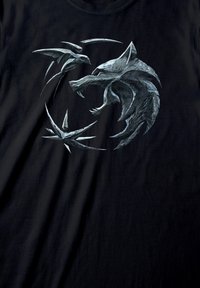 Sort t-shirt med et detaljeret, gråmetal wolf-design omgivet af skarpe, vinkelformede accenter. Stoffet virker blødt med en let tekstur.