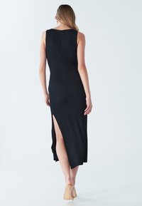 Svart ärmlös klänning med figurnära passform och en slits på sidan. Tillverkad av texturerat tyg med subtil glans och dragkedja baktill.