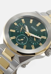 Silberne und goldene Edelstahl-Armbanduhr mit einem grünen strukturierten Zifferblatt, goldenen Stundenmarkierungen und zwei Unterzifferblättern. Verfügt über ein kantiges Gehäusedesign.