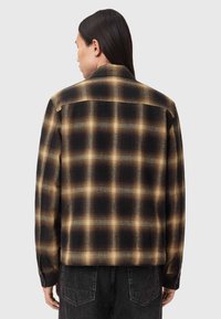 Camicia a quadri nera e marrone con una texture liscia, yoke posteriore e polsini con bottoni. Presenta una vestibilità rilassata e due pieghe posteriori per maggiore comodità.